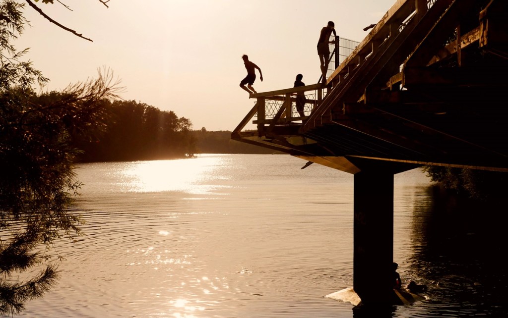 Menschen springen bei Sonnuntergang von Brücke in See